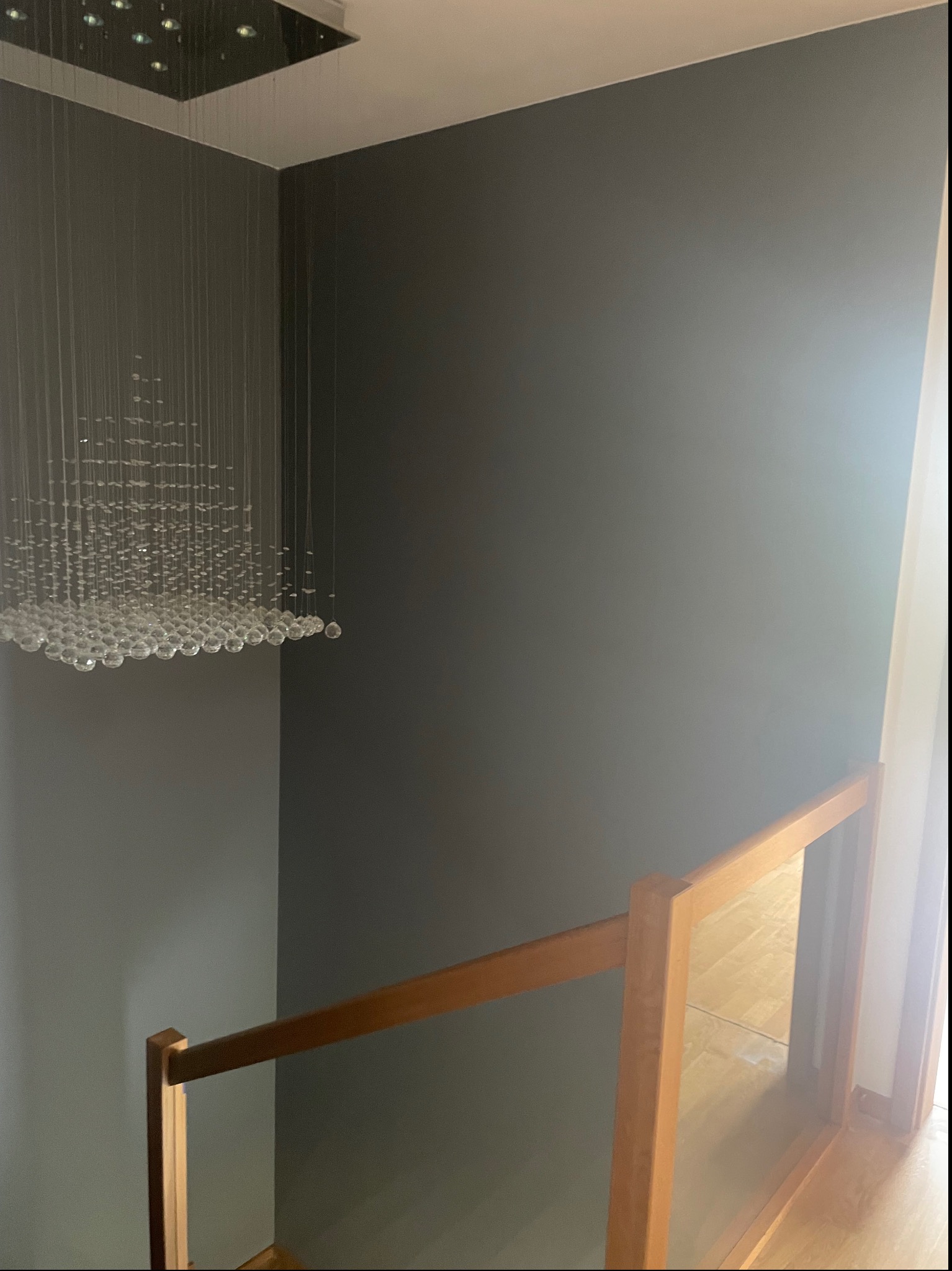 Ściana pomalowana na szaro w korytarzu ze szklaną balustradą i nowoczesnym żyrandolem z kryształków.