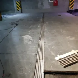 Betonowa podłoga w garażu z zamontowanym odpływem liniowym i przygotowanymi drewnianymi elementami do montażu, widoczne ślady po pracach budowlanych.