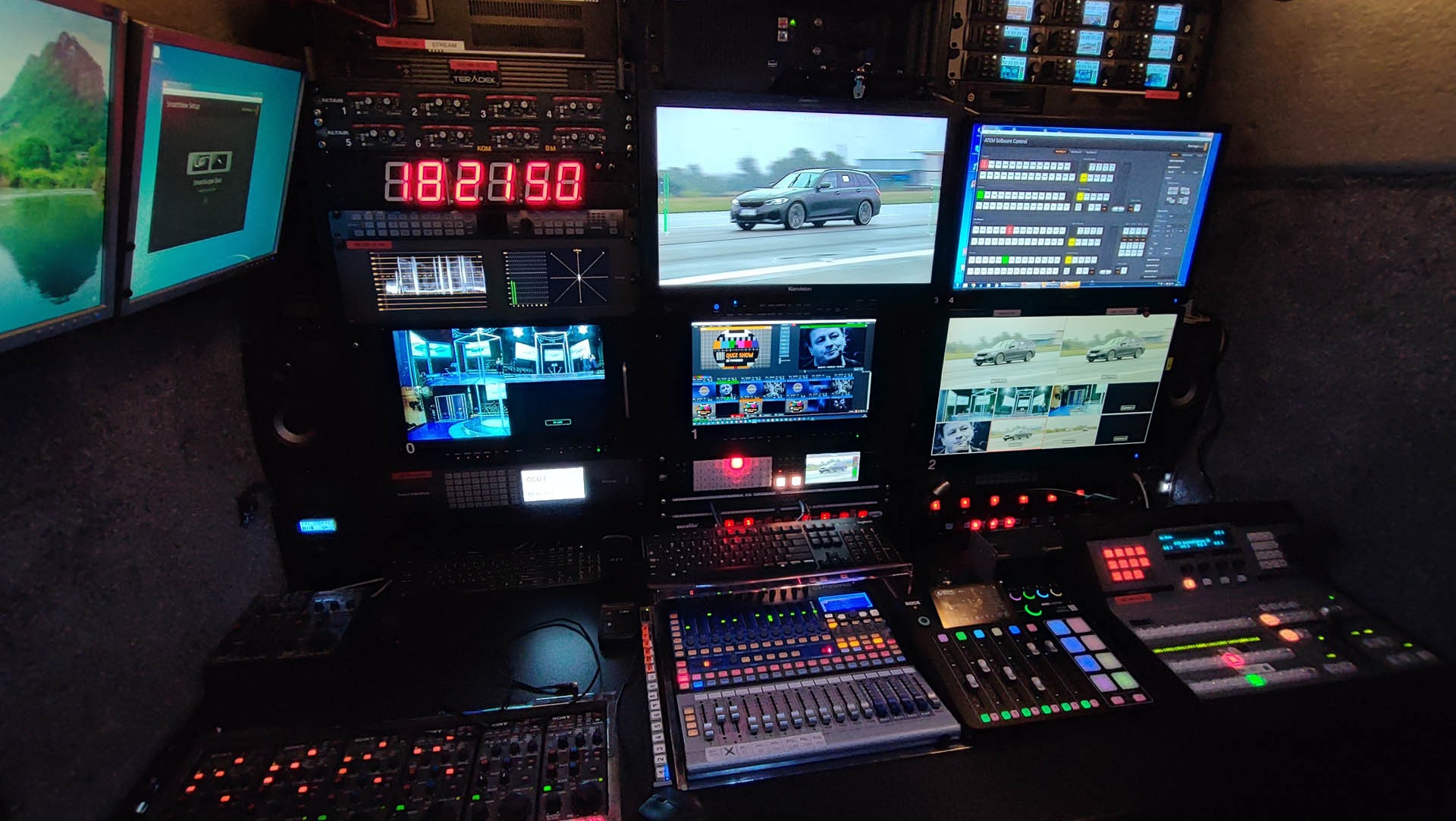 Stanowisko reżyserskie z wieloma monitorami pokazującymi różne ujęcia, mikserem audio i kontrolerami wideo, w tle wyświetlany obraz górski na monitorze.