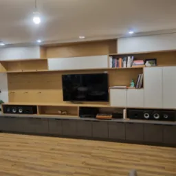 Zabudowa meblowa na wymiar w salonie z szafkami w kolorze szarym i białym, otwarte półki z drewnianym fornirem, sprzęt audio-wideo i dekoracje.