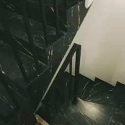 Schody wewnętrzne z czarnego marmuru z metalową, czarną balustradą, widok z góry, oświetlenie górne.