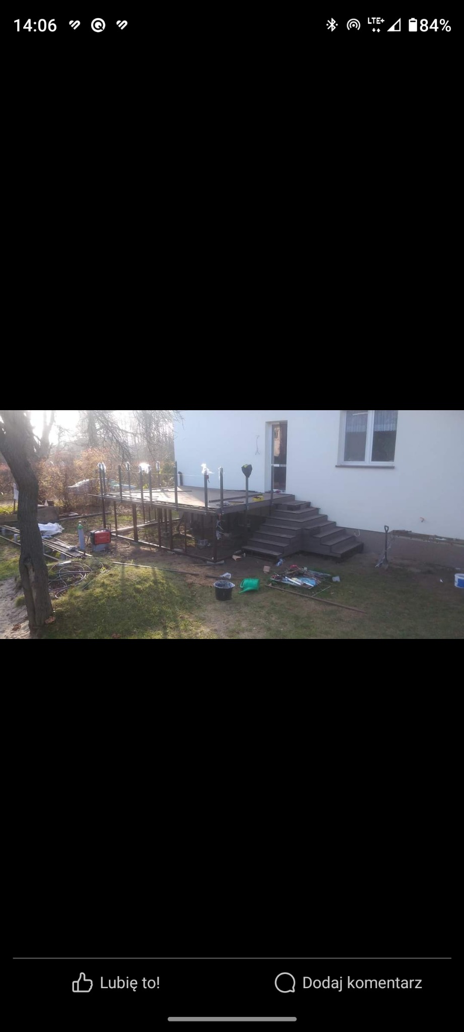 Konstrukcja pod taras z metalowymi słupkami i częściowo zamontowanymi poręczami, widoczna w trakcie budowy przy domu z betonowymi schodami.