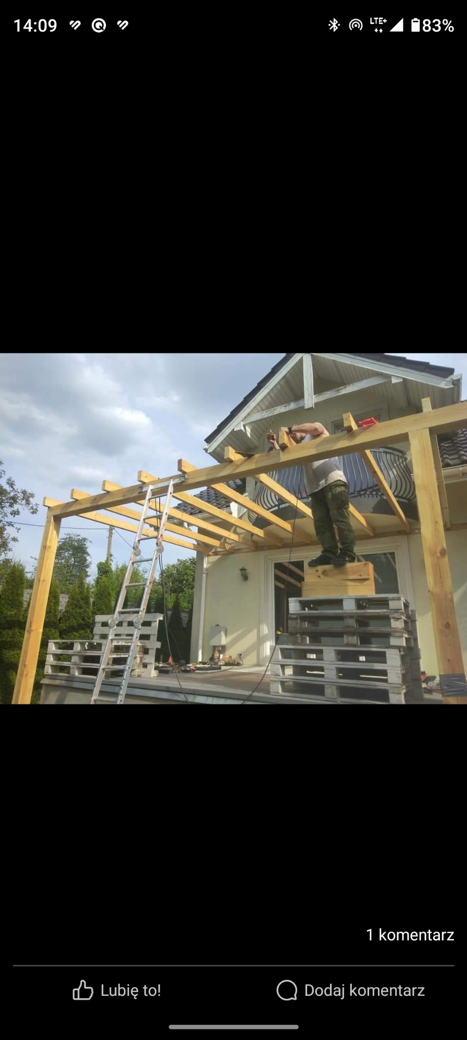 Montaż drewnianej konstrukcji z belek na tarasie domu jednorodzinnego, widoczna drabina i mężczyzna pracujący na wysokości.