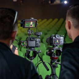 RAFAELLO FILM RAFAŁ MAĆKOWIAK - Dwaj mężczyźni obserwują nagrywanie wideo z kobietą na zielonym tle, widoczne na monitorach kamer i dodatkowym ekranie podglądowym.