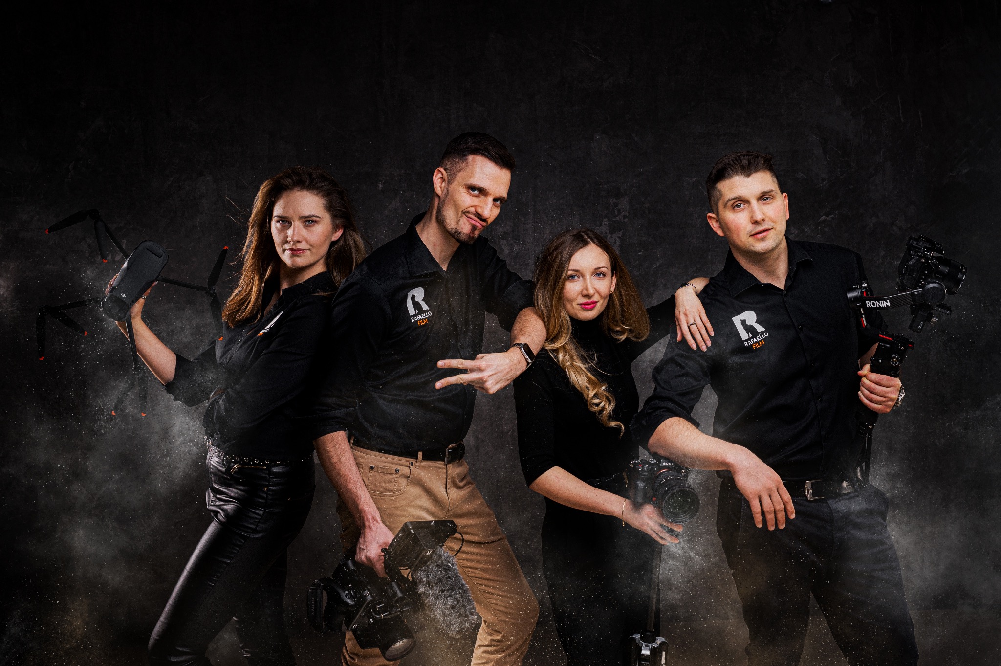Zespół filmowy w czarnych koszulach z logo 'Rafaello Film' pozuje z dronem, kamerami i stabilizatorem Ronin na tle ciemnego, teksturowanego tła.