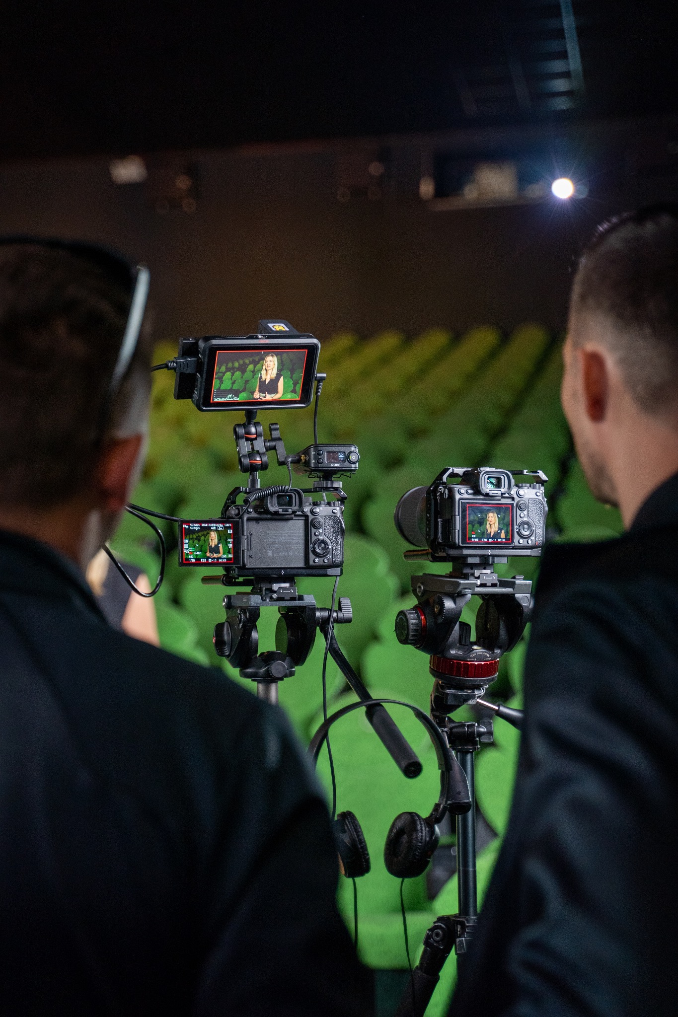 Dwaj mężczyźni obserwują nagrywanie wideo z kobietą na zielonym tle, widoczne na monitorach kamer i dodatkowym ekranie podglądowym.