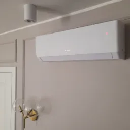 Biały klimatyzator marki Gree zamontowany na ścianie w pomieszczeniu z dekoracyjną sztukaterią i lampą ścienną z dwoma szklanymi kloszami.