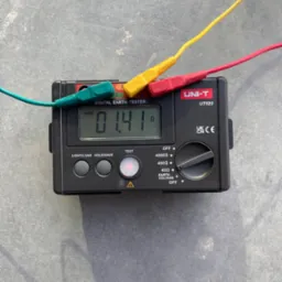 Czarny miernik rezystancji uziemienia UNI-T UT522 z trzema przewodami zakończonymi krokodylkami (zielony, ż&oacute;łty, czerwony) podłączonymi do urządzenia, wyświetlający wynik pomiaru 0.14 &Omega; na szarym tle.