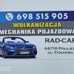 Szyld reklamowy warsztatu samochodowego z numerem telefonu, adresem i zdjęciem niebieskiego kabrioletu marki Mercedes.