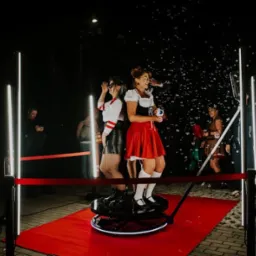 Dwie kobiety w przebraniach pozują na platformie obrotowej, otoczone bańkami mydlanymi i oświetleniem LED, podczas wieczornego wydarzenia.