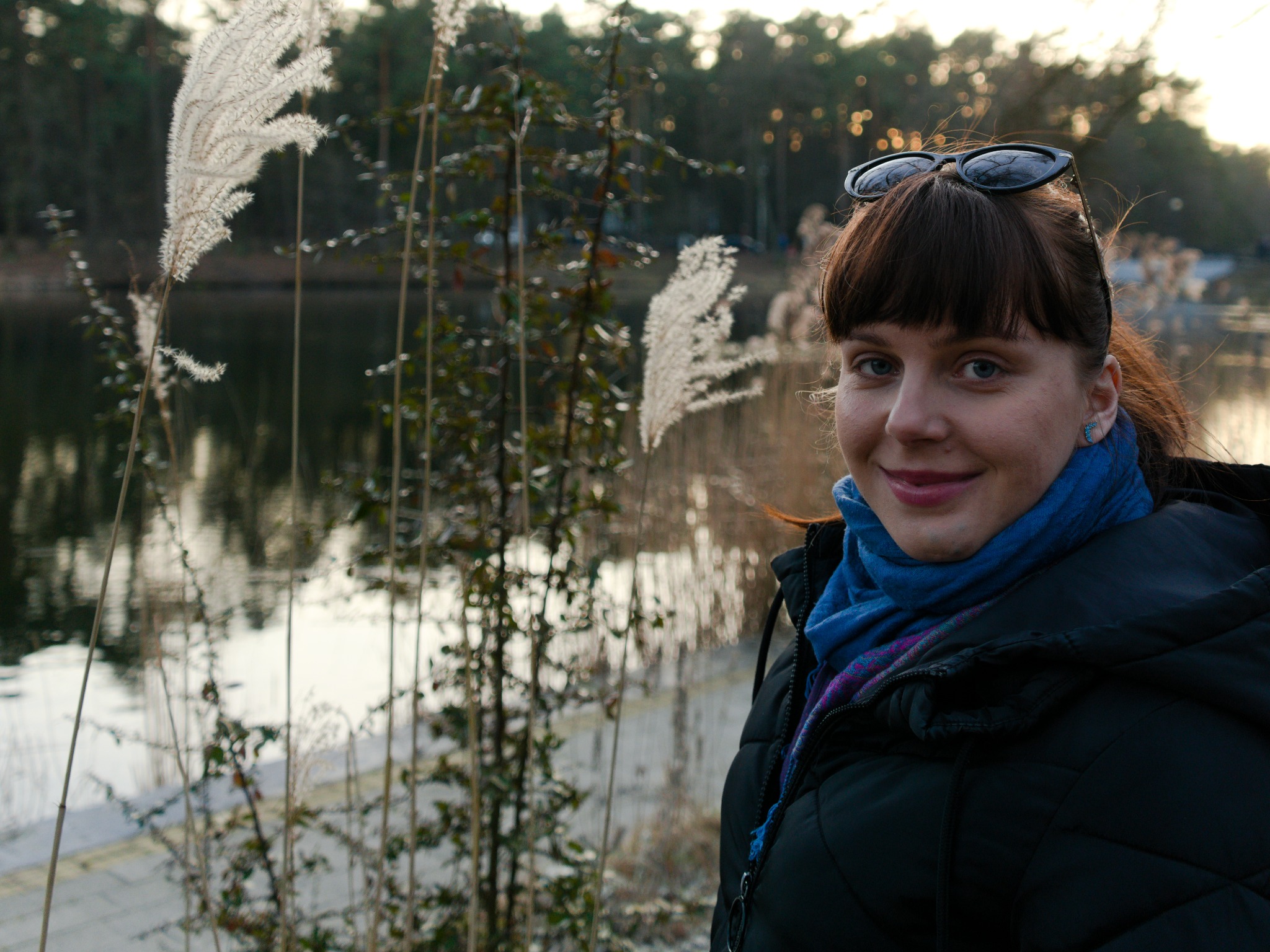 Portret uśmiechniętej kobiety z okularami na głowie, w tle jezioro i trzciny