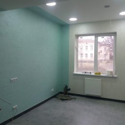 VELVET MIX DECORBUD Yurii Raba - Wnętrze pokoju po malowaniu ścian na dwa kolory: miętowy i jasny beż, z szarą podłogą z płytek, grzejnikiem pod oknem i piłą do cięcia paneli przypodłogowych w rogu.