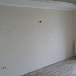 VELVET MIX DECORBUD Yurii Raba - Pomalowane ściany w odcieniach beżu z widocznymi gniazdkami elektrycznymi i panelami na podłodze, surowy sufit i wisząca żarówka.