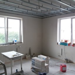 VELVET MIX DECORBUD Yurii Raba - Wnętrze w trakcie montażu sufitu podwieszanego w Warszawie, widoczne profile metalowe, narzędzia i materiały budowlane, surowe ściany przygotowane do dalszych prac wykończeniowych.