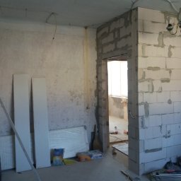 VELVET MIX DECORBUD Yurii Raba - Wnętrze w trakcie budowy: ściany z betonu komórkowego, widoczne instalacje elektryczne, worki z zaprawą, grzejniki w folii i narzędzia na podłodze