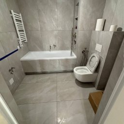 VELVET MIX DECORBUD Yurii Raba - Nowoczesna łazienka wykończona płytkami imitującymi marmur, z wiszącą toaletą, wanną i grzejnikiem drabinkowym, oświetlona górnym światłem.