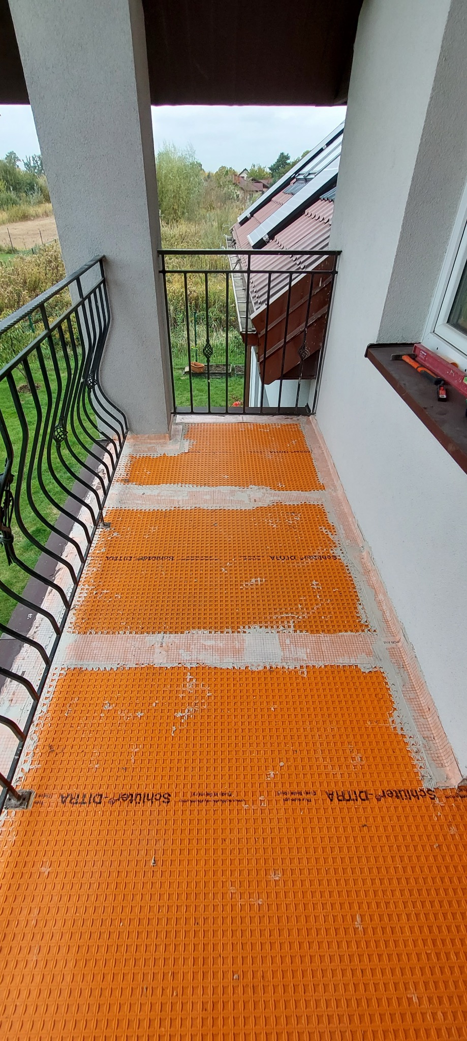Pomarańczowa mata drenażowa Schluter-DITRA ułożona na podłodze balkonu, przygotowana pod dalsze prace wykończeniowe.