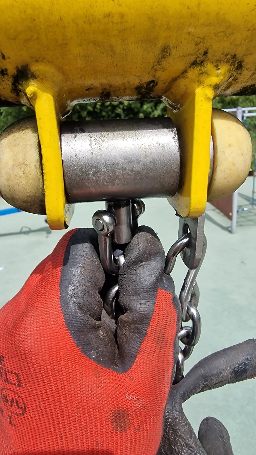 Dłoń w roboczej rękawicy łączy łańcuch do żółtej konstrukcji w Kazimierzy Wielkiej, prawdopodobnie element instalacji podwieszanej.