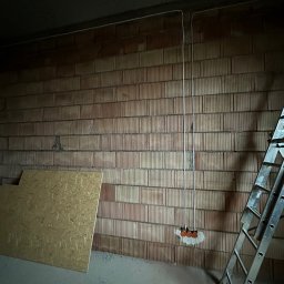 LANRUNNER Mateusz Sałek - Surowa ściana z cegły dziurawki z poprowadzonymi przewodami elektrycznymi i puszkami pod gniazdka, obok drabina aluminiowa, na podłodze płyta OSB.