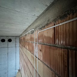 LANRUNNER Mateusz Sałek - Instalacja elektryczna: białe przewody ułożone wzdłuż ceglanej ściany pod betonowym sufitem w surowym stanie.