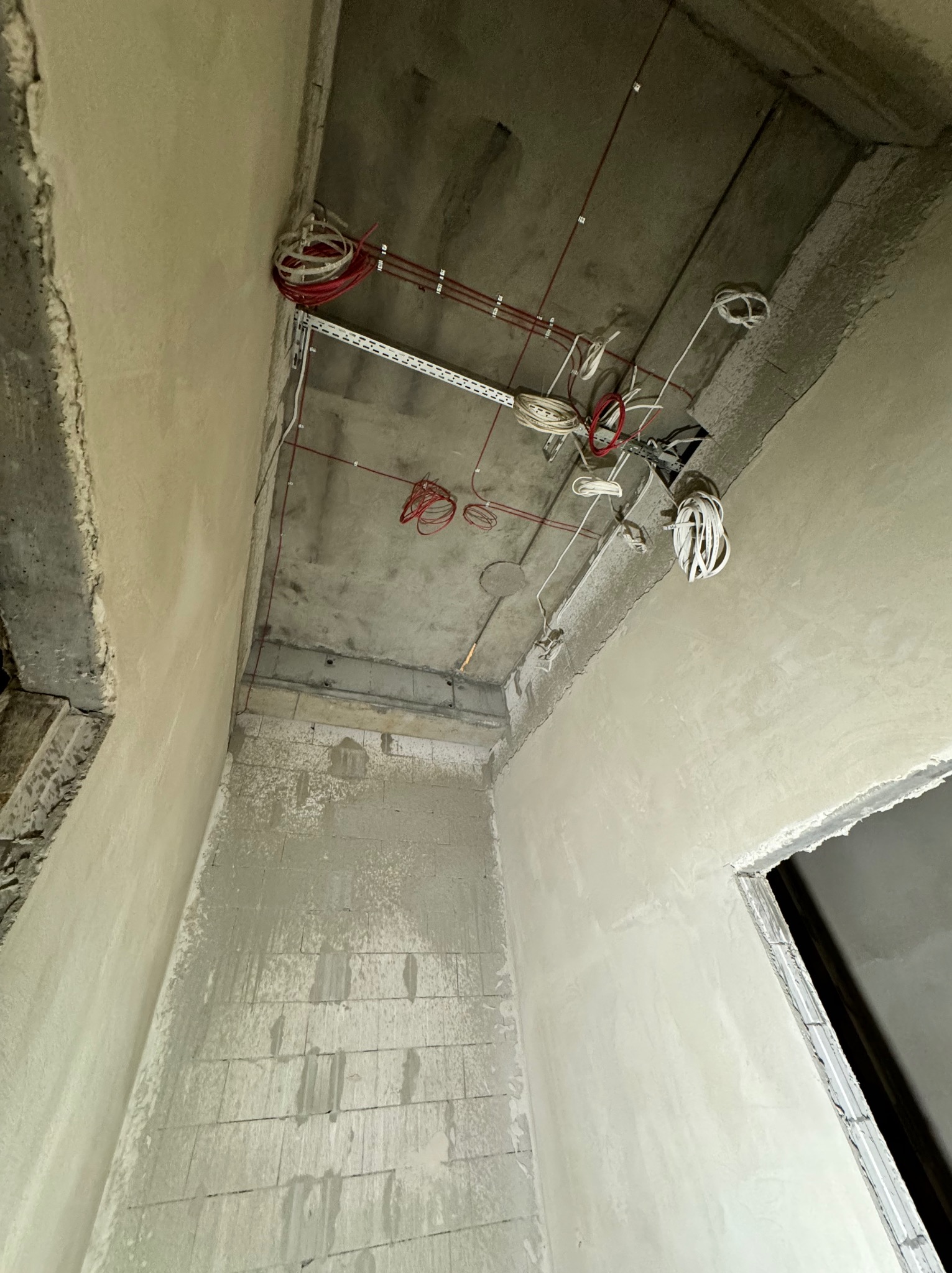 Surowy stan wnętrza w trakcie remontu: widoczne przewody elektryczne wystające z sufitu, ściany w trakcie tynkowania, surowy betonowy strop z elementami instalacji elektrycznej.