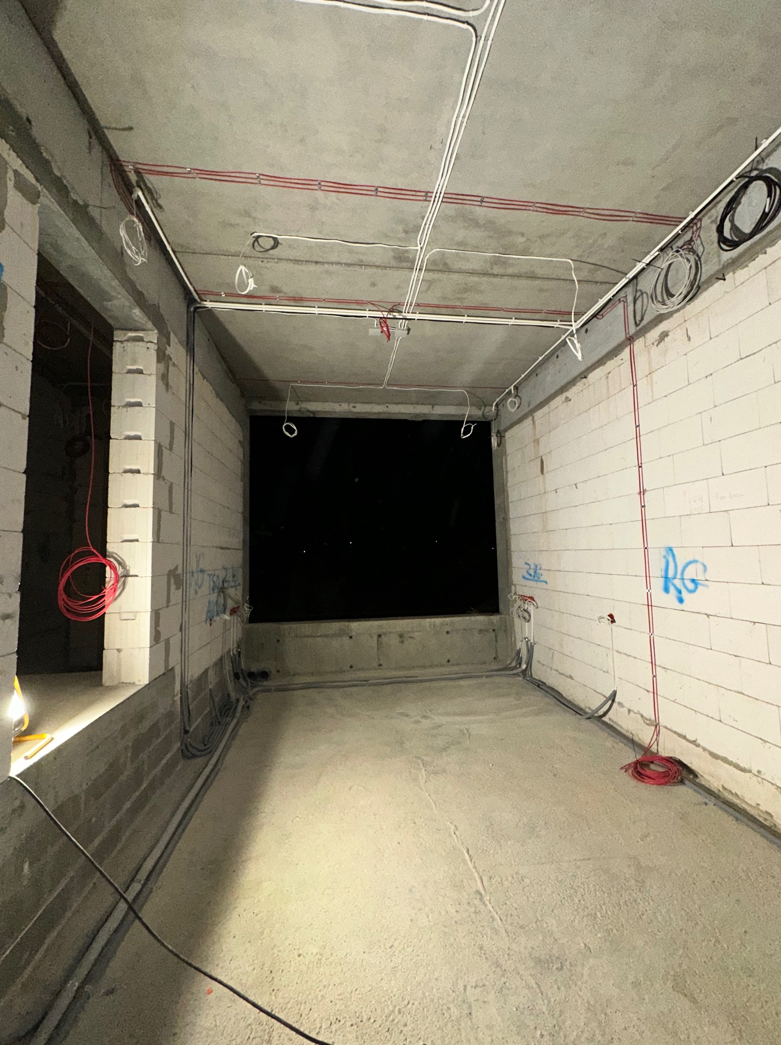 Surowy stan wnętrza w trakcie prac: widoczne przewody elektryczne prowadzone po suficie i ścianach z betonu komórkowego, brak wykończeń.