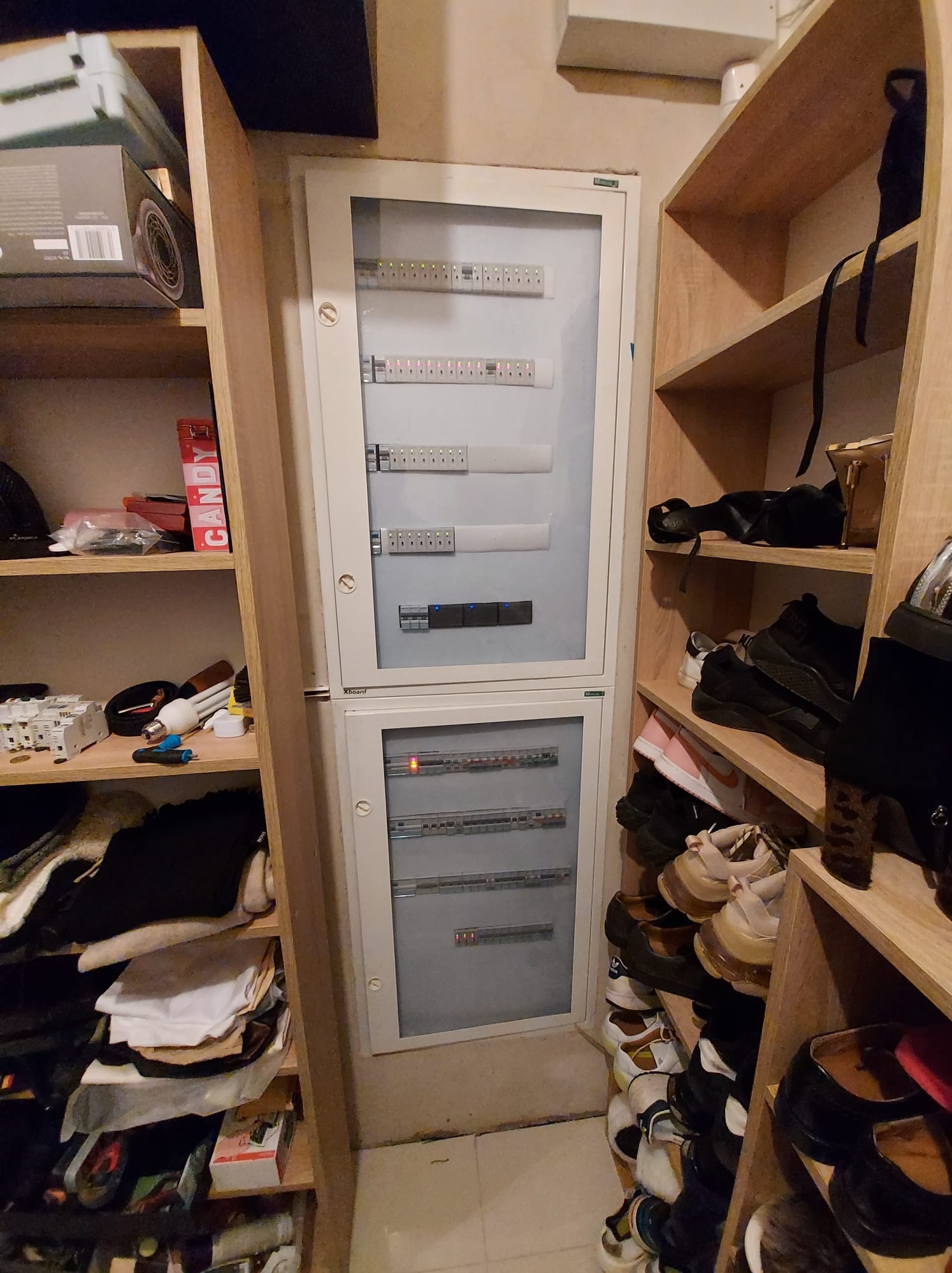 Rozdzielnica elektryczna z zabezpieczeniami, umieszczona w szafie wnękowej, obok półek z ubraniami i innymi przedmiotami.