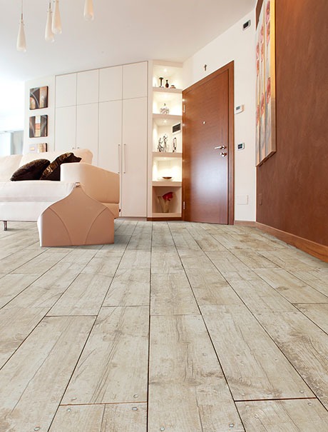 Jasna, drewnopodobna podłoga w salonie z beżową sofą i szafą w zabudowie, widok na otwarte drzwi i dekoracje ścienne.