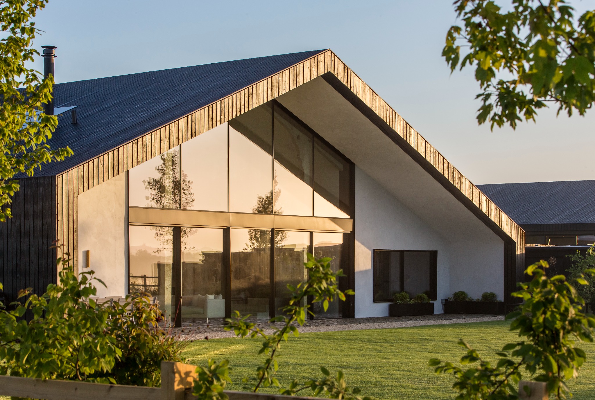Nowoczesny dom z dużymi przeszkleniami, drewnianą elewacją i dachem w kolorze antracytu, widok z ogrodu w słoneczny dzień.