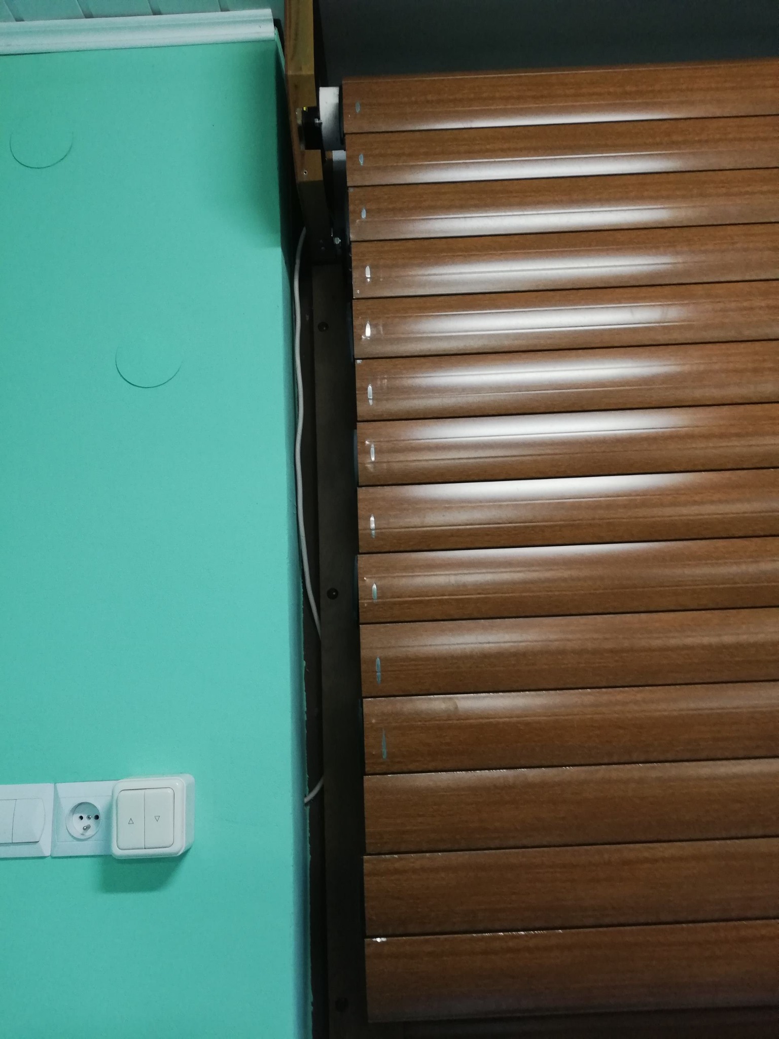 Brązowa roleta zewnętrzna zamontowana na tle turkusowej ściany z widocznym gniazdkiem i włącznikiem w Bytomiu.