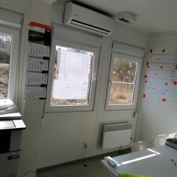 Clean&KlimaKing - Wnętrze biura kontenerowego z zamontowaną klimatyzacją Kaisai, kalendarzem na ścianie i planami budowlanymi przyklejonymi taśmą do okna.