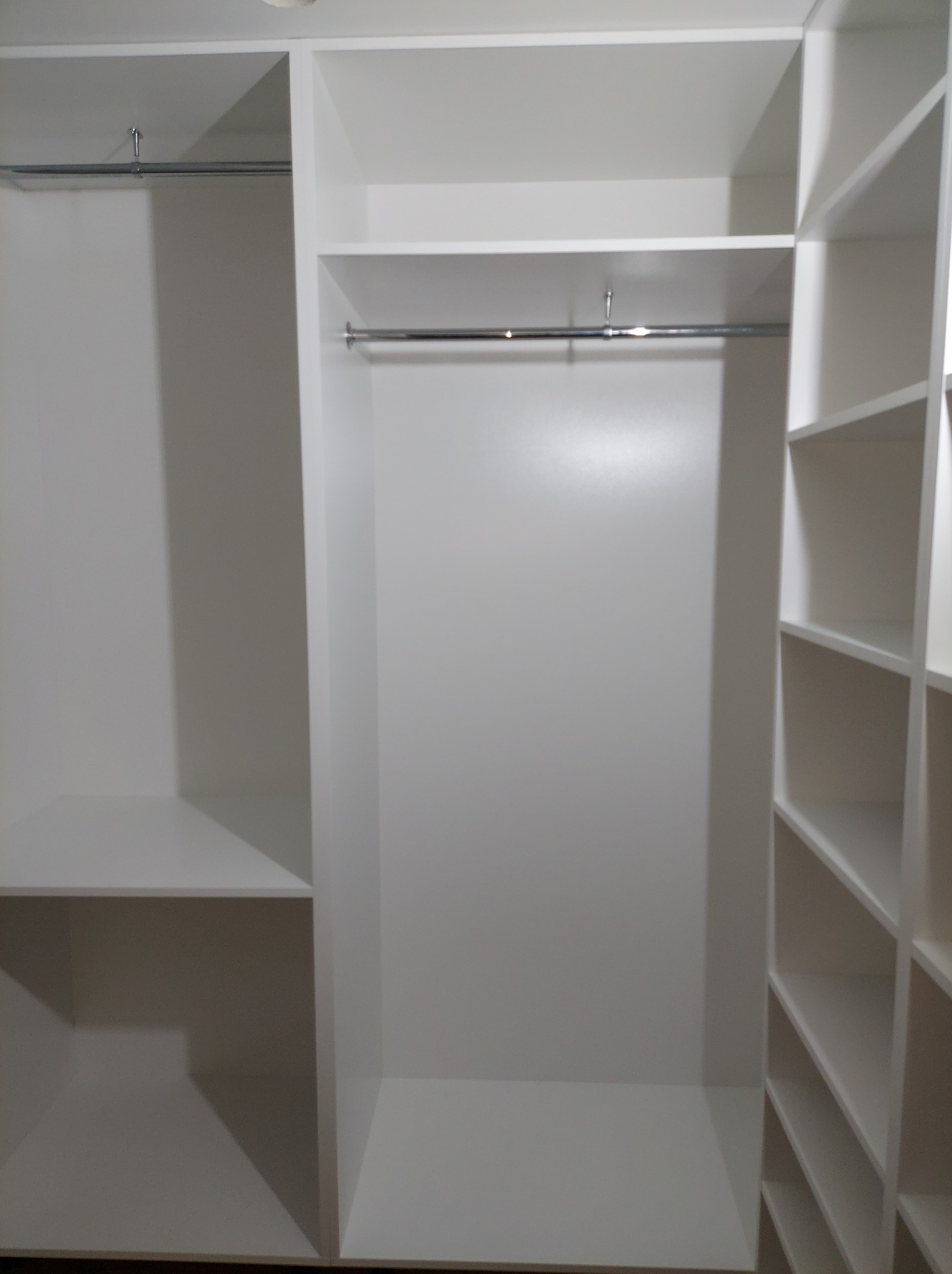 Wnętrze białej szafy wnękowej z drążkami na ubrania i półkami po prawej stronie