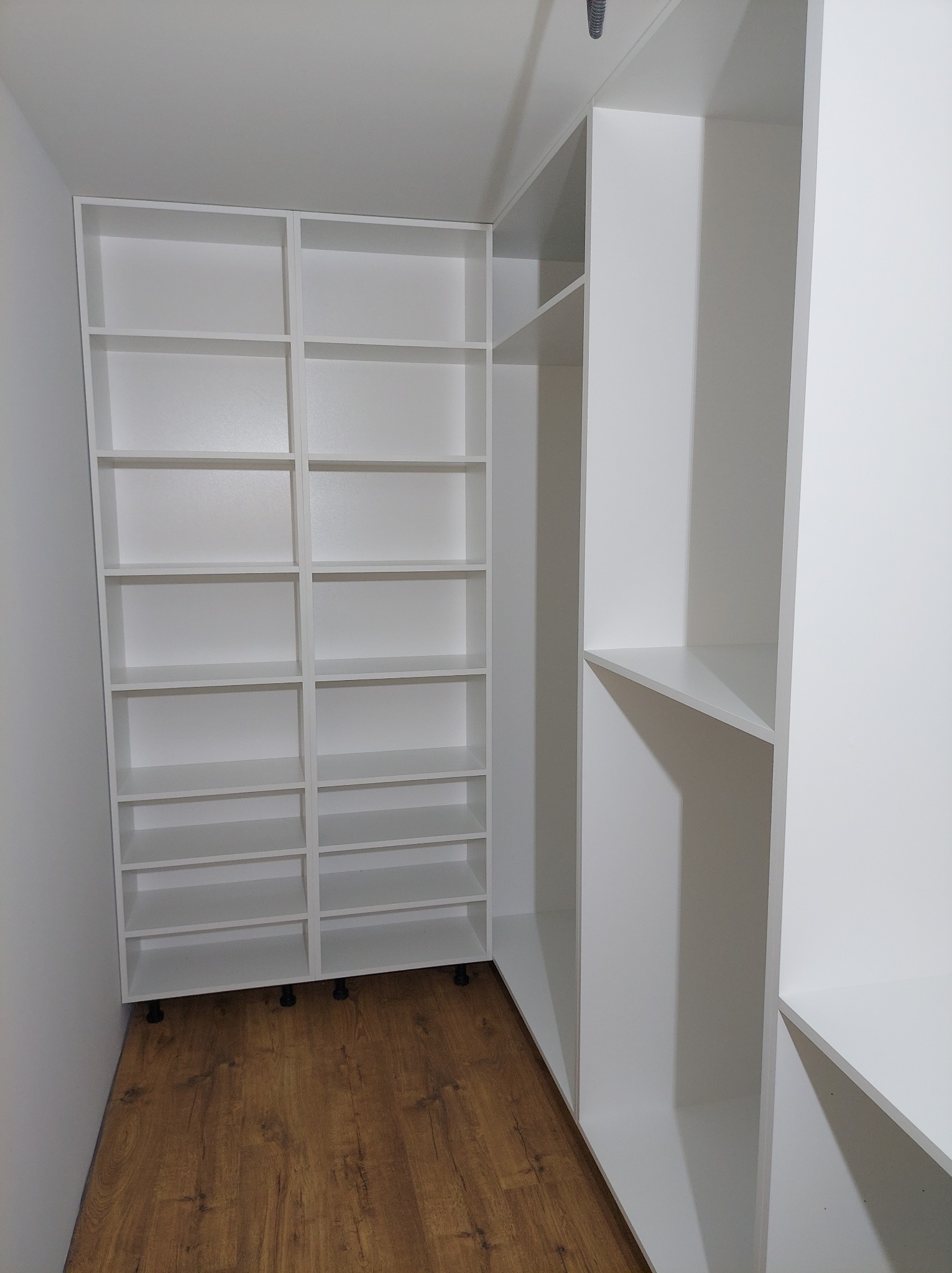 Biała szafa wnękowa z półkami, widoczna na drewnianej podłodze z bliska, z perspektywy wnętrza szafy.