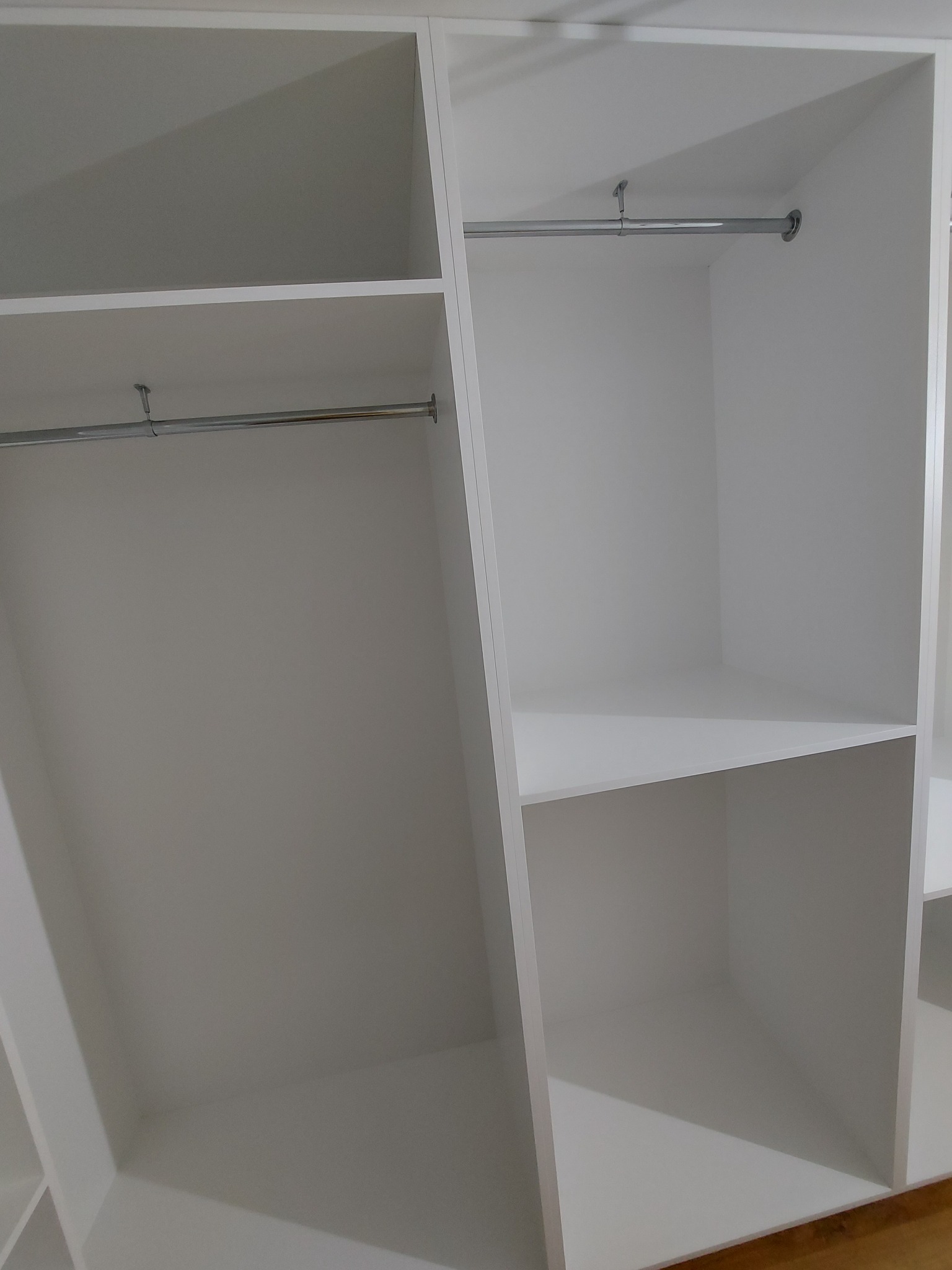 Wnętrze białej szafy z półkami i drążkami na ubrania, widok z góry, minimalistyczny design.