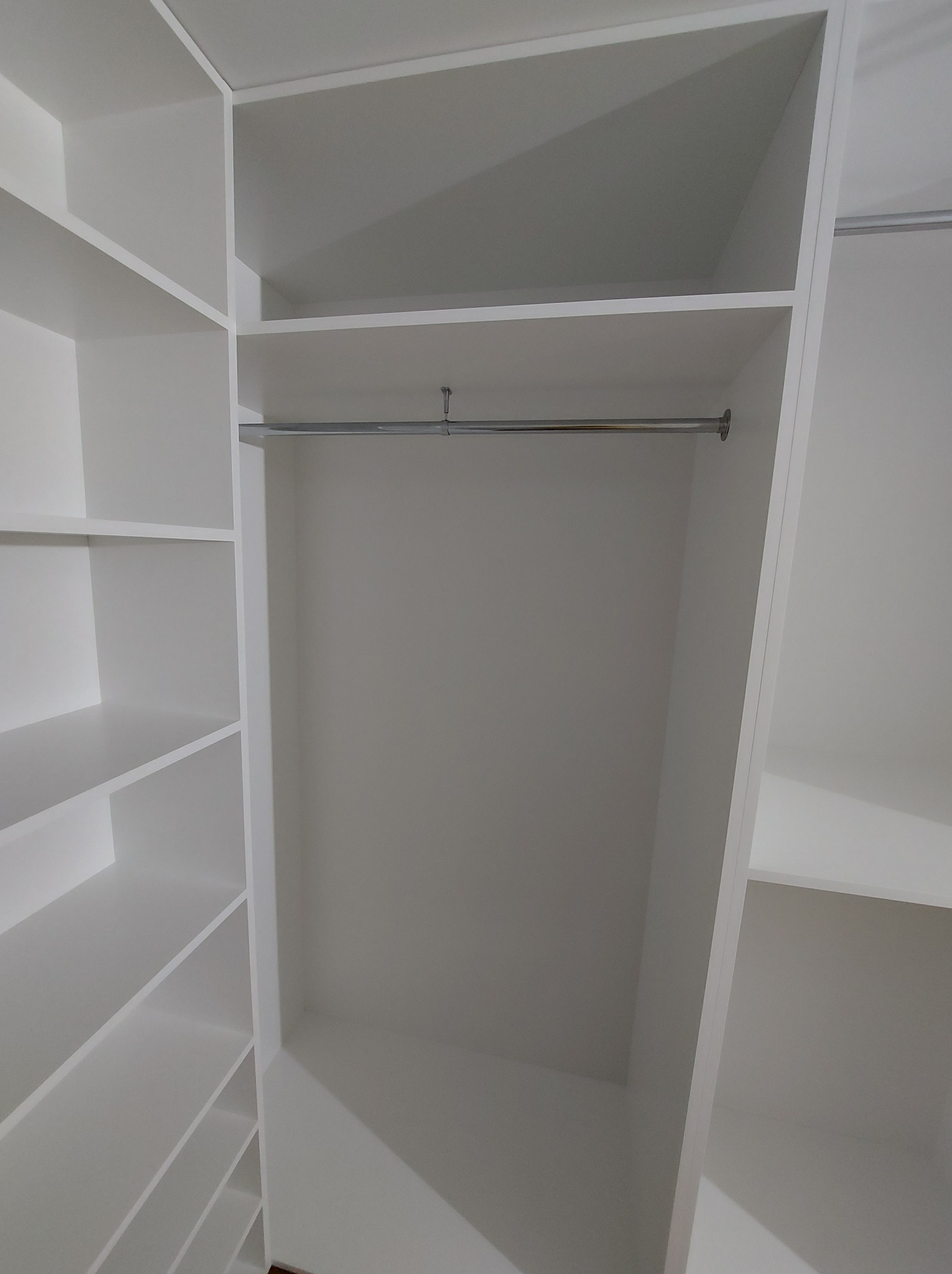 Wnętrze białej, minimalistycznej szafy wnękowej z drążkiem na ubrania i półkami po lewej stronie.