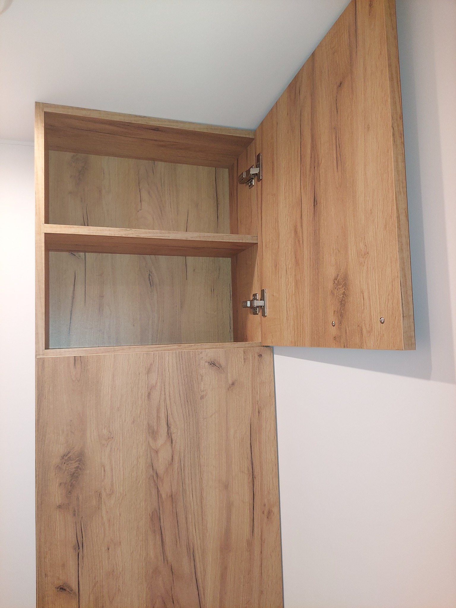 Otwarta szafka wisząca z półkami, imitacja drewna, widoczne zawiasy.