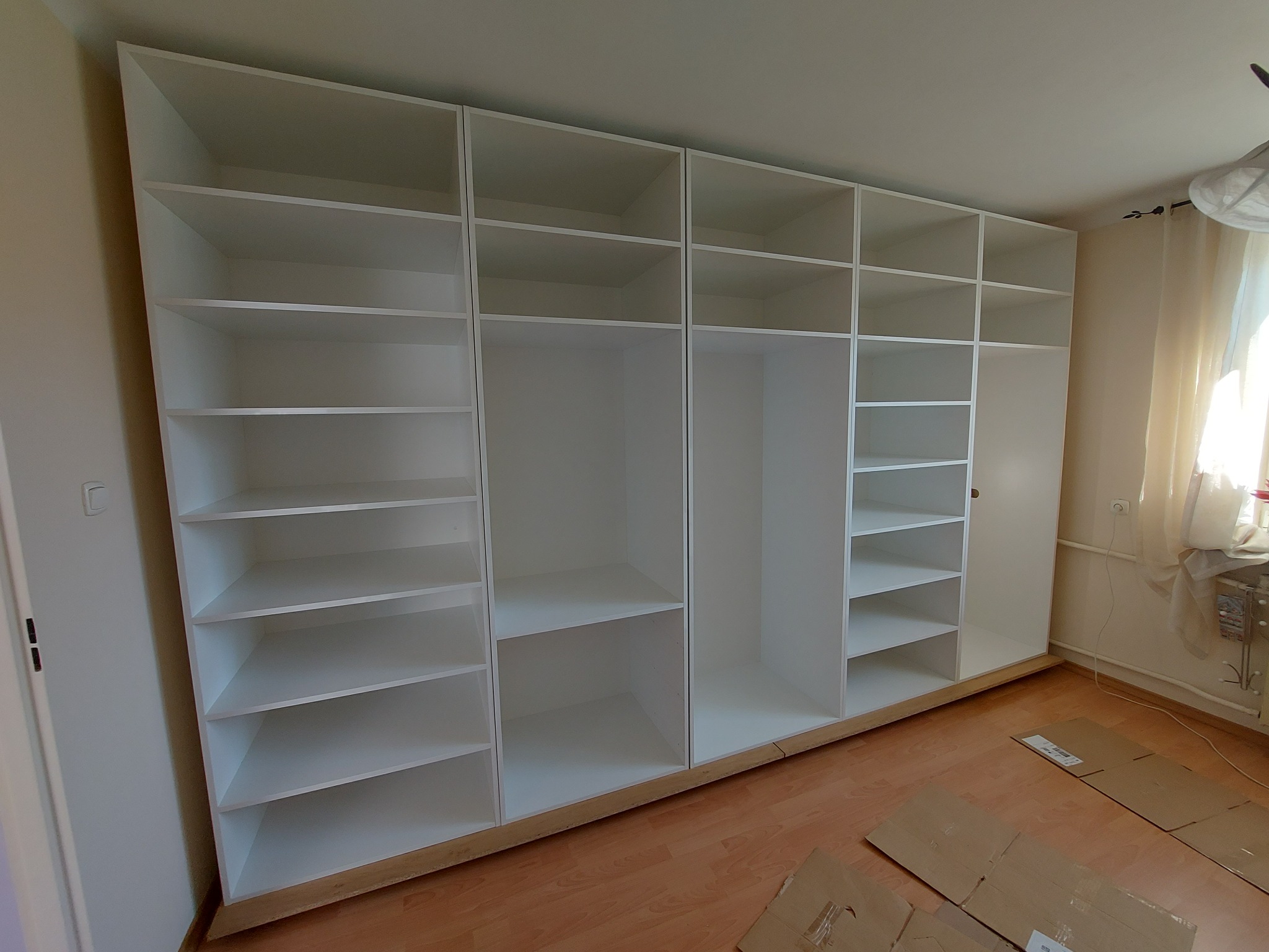 Biała, modułowa szafa wnękowa z półkami i przestrzenią na wieszaki, widok z perspektywy. Realizacja w Nosówce. Minimalistyczny design, jasne wnętrze.