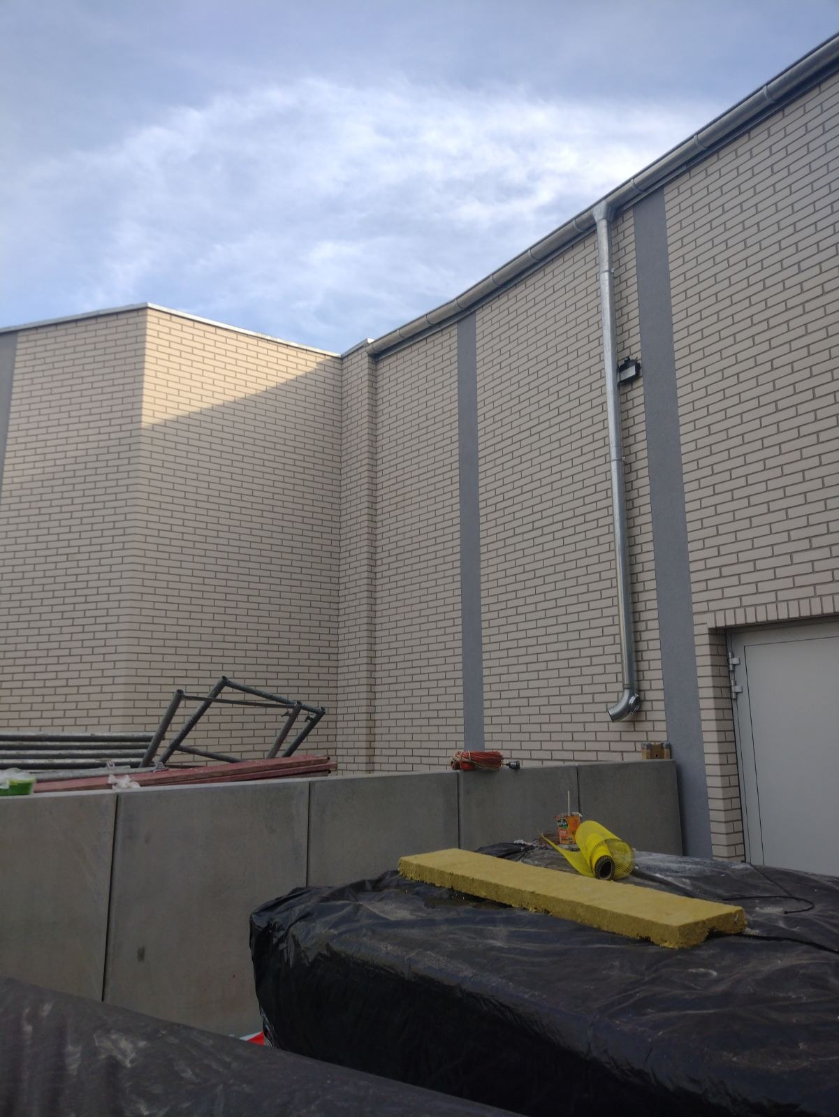 Fragment ocieplonej ściany budynku z jasnej cegły z widocznym rusztowaniem, materiałami izolacyjnymi i rynną spustową