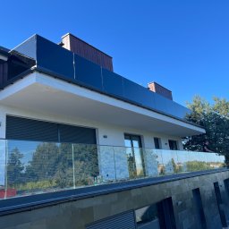 METAL-CHROM - Nowoczesny budynek z balkonem i szklaną balustradą, widok z dołu na błękitne niebo, z widocznymi narzędziami i materiałami budowlanymi na balkonie.