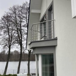 METAL-CHROM - Nowoczesny balkon z prostą, stalową balustradą na tle jeziora i nagich drzew, widoczne elementy elewacji domu i prace brukarskie w ogrodzie.