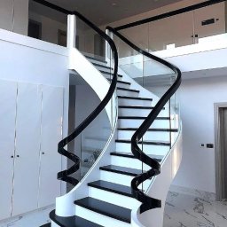 METAL-CHROM - Eleganckie, spiralne schody z czarnymi stopniami i białą konstrukcją, otoczone szklaną balustradą z czarnymi poręczami, w przestronnym, nowoczesnym wnętrzu z marmurową podłogą.