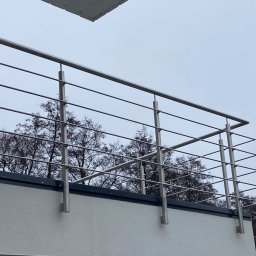 METAL-CHROM - Nowoczesna balustrada nierdzewna z poziomymi prętami na balkonie, widok z dołu, na tle drzew bez liści i pochmurnego nieba.