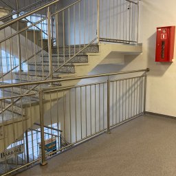 METAL-CHROM - Klatka schodowa w budynku użyteczności publicznej z betonowymi schodami i metalową balustradą, widoczna skrzynka przeciwpożarowa na ścianie.