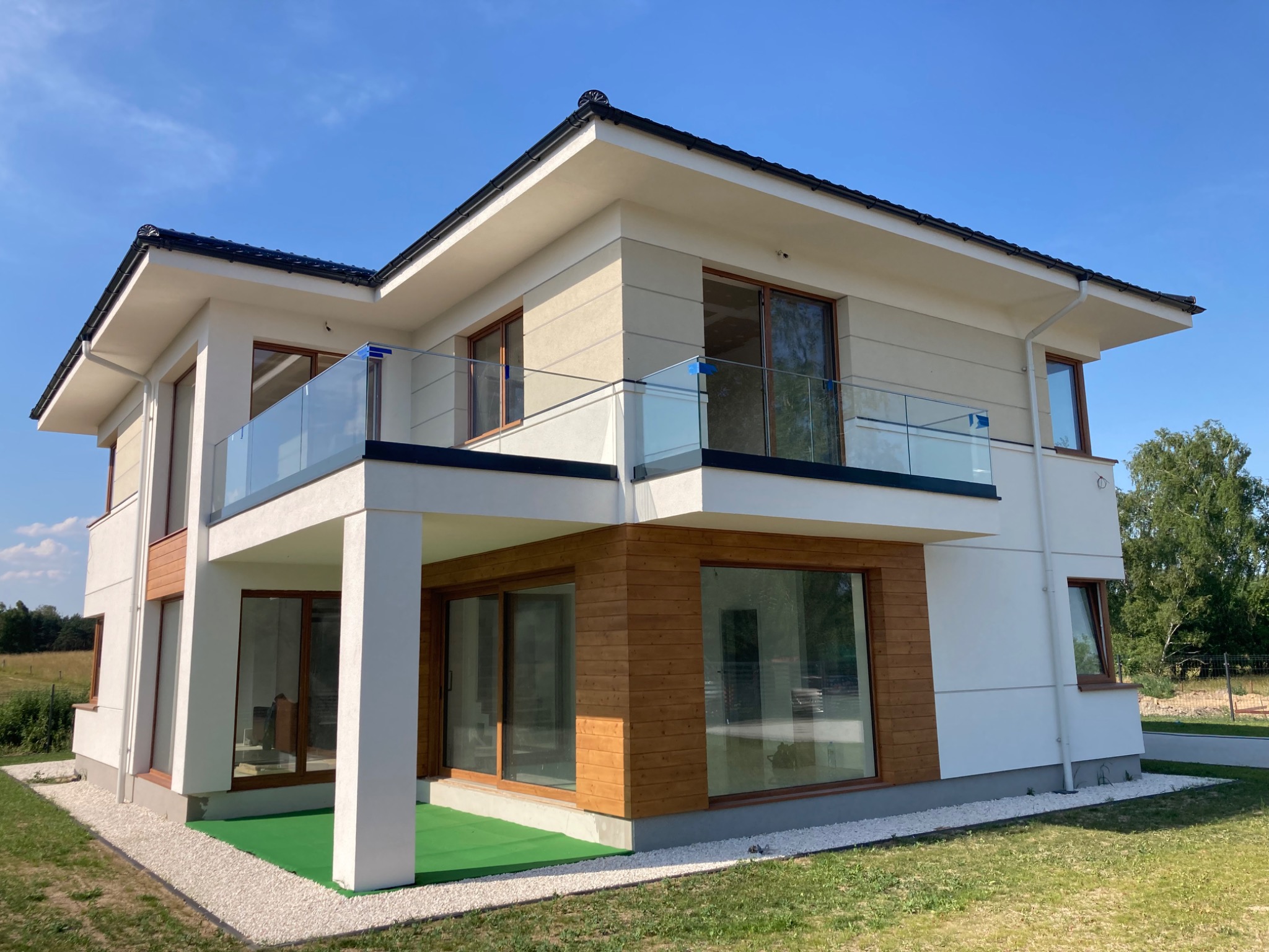 Nowoczesny dom z balkonami zabezpieczonymi przezroczystą balustradą szklaną, widok z zewnątrz w słoneczny dzień.