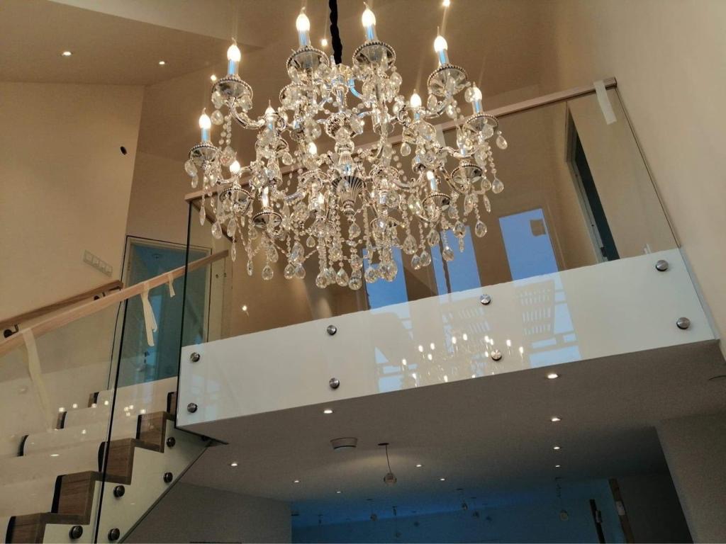 Szklana balustrada schodowa z drewnianymi stopniami i kryształowym żyrandolem w tle, widok od dołu.