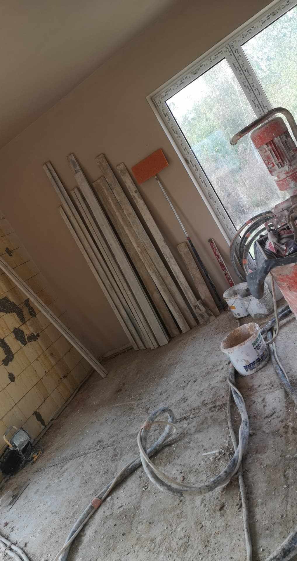 Przygotowanie do prac tynkarskich w Świebodzinie: widoczna maszyna do tynkowania, listwy przypodłogowe, wiadro i akcesoria na zakurzonym podłożu w pomieszczeniu z otynkowanymi ścianami.