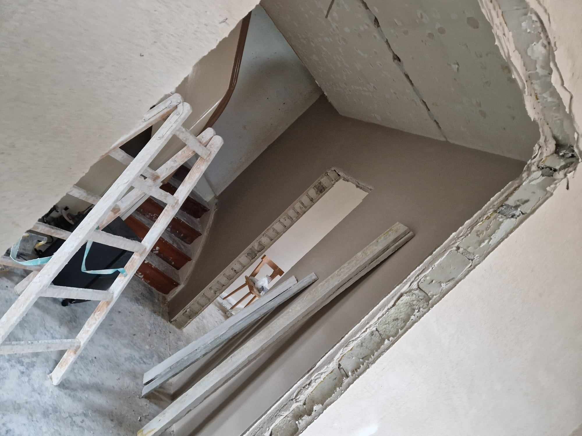 Wnętrze w trakcie prac tynkarskich: widoczne świeżo otynkowane ściany, drewniana drabina oparta o schody, oraz fragmenty niezabezpieczonych, surowych ścian.