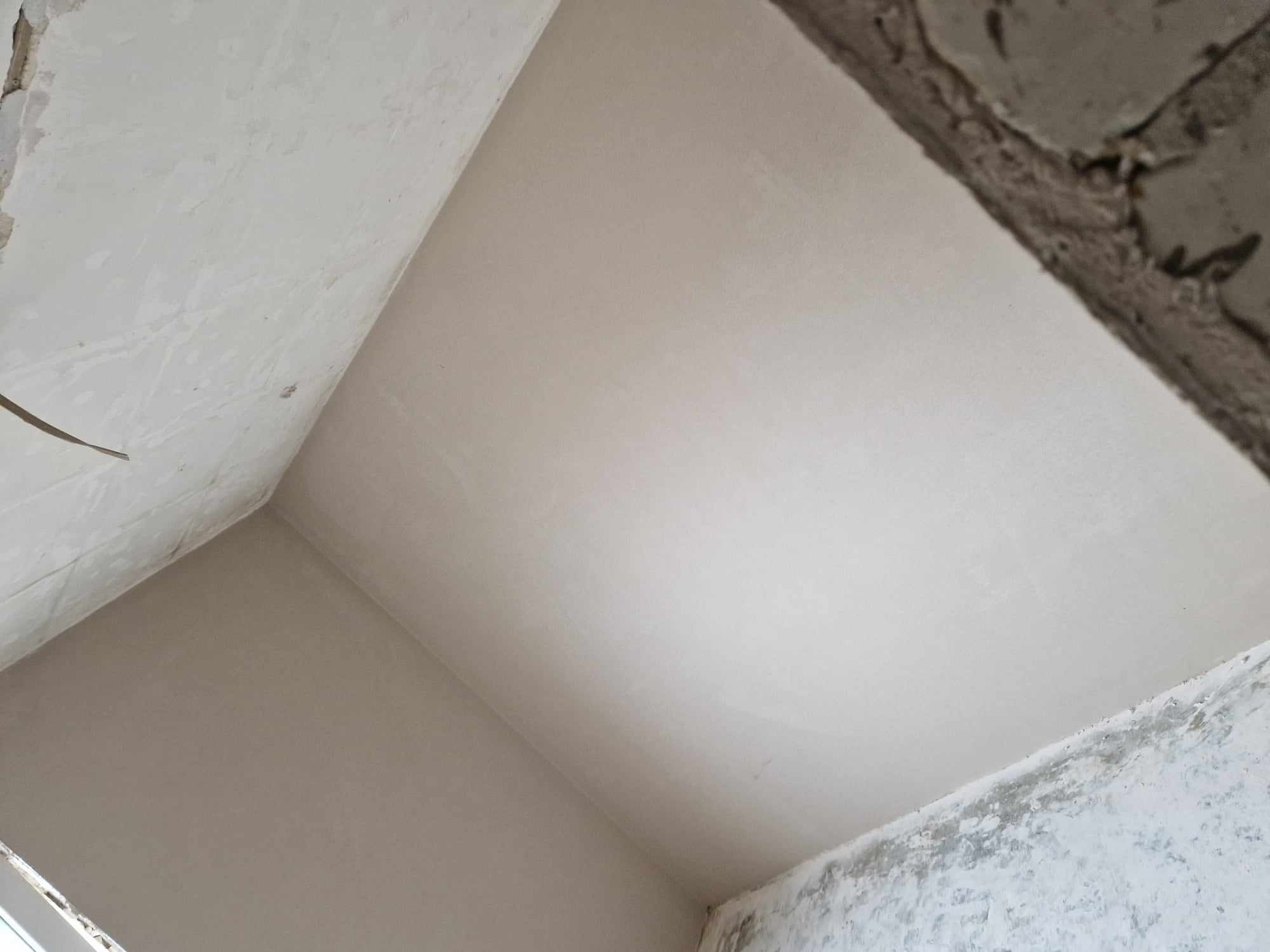 Świeżo nałożone tynki maszynowe na ścianach i suficie, widoczne surowe wykończenia i fragmenty starego tynku.