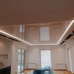 Nowoczesny salon po remoncie: podwieszany sufit z oświetleniem LED, ściana z cegły, okna z roletami. Częściowo zakryty mebel folią ochronną.