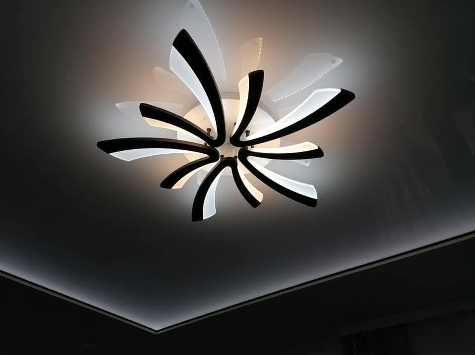 Nowoczesna lampa sufitowa LED w kształcie kwiatu z czarno-białymi elementami, oświetlająca sufit z listwą LED. Minimalistyczny design.